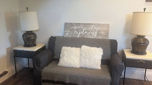 A cozy seating area with a grey sofa, two decorative lamps, a map with 'Verve exploring' text, and a small side table. - Entire Private one Bedroom Apartment Alton, Ont (Caledon)