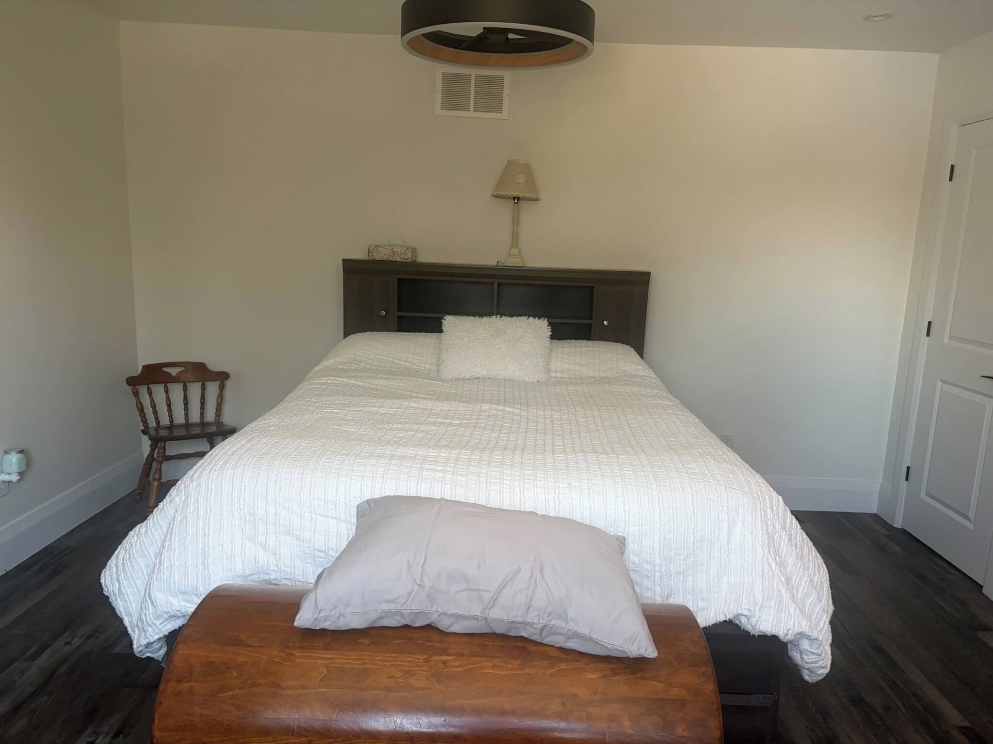 Un dormitorio con una cama grande, un banco de madera, una mesita de noche, una lámpara y una lámpara de techo.