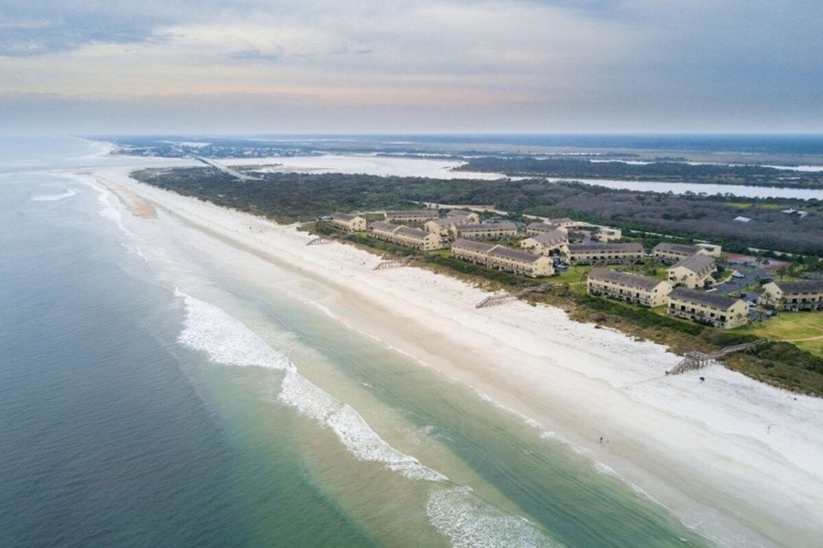 An aerial view of a coastal hotel with multiple buildings, a beach, and a view of the ocean.