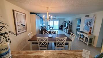 A dining area with a marble table and white chairs, a chandelier, and a view into the living room.