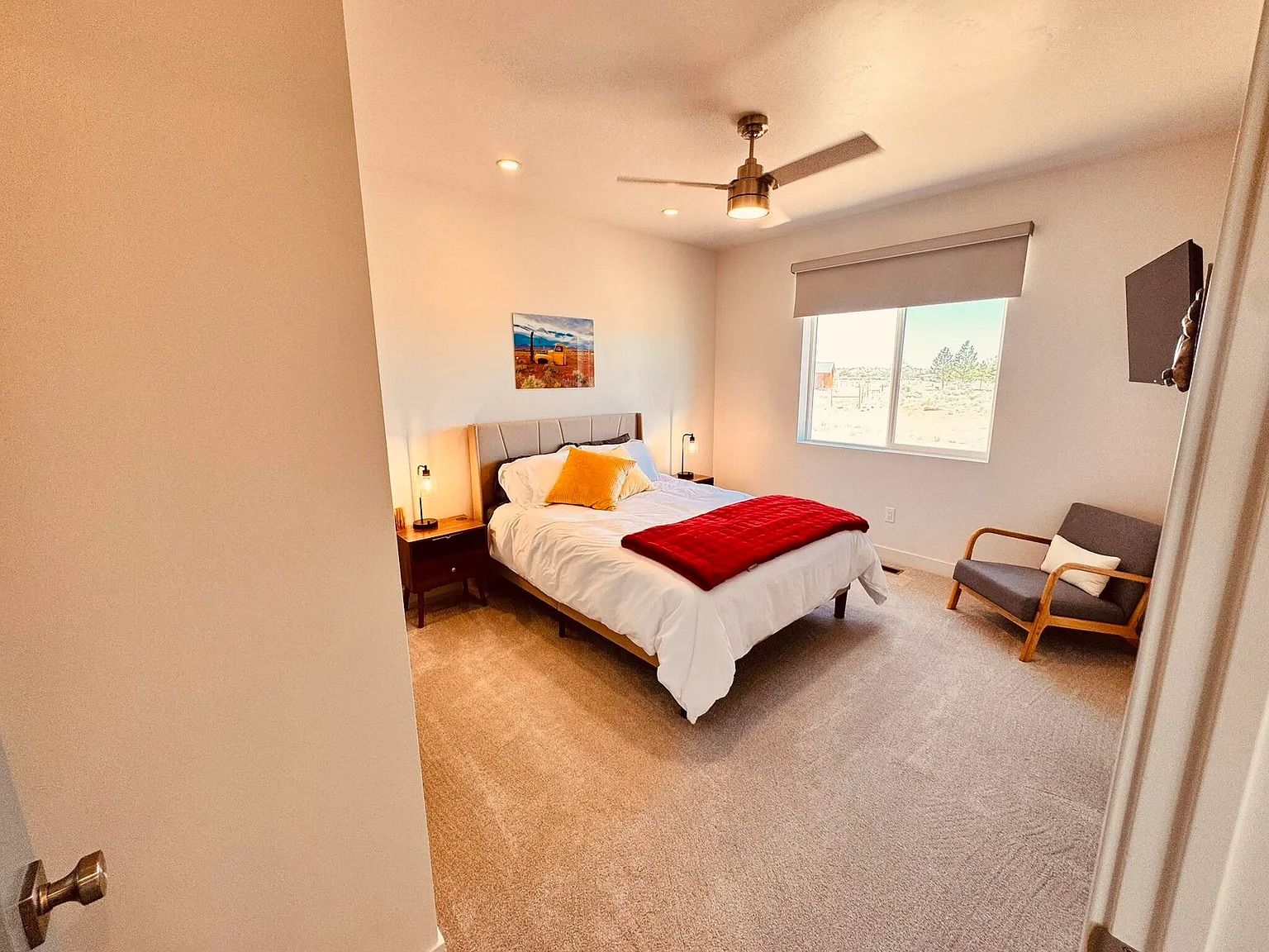 Ein Schlafzimmer mit Bett, Sessel, Deckenventilator, Fenster und einem Gemälde an der Wand.