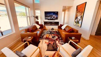 Ein modernes Wohnzimmer mit Ledersofas, einem Flachbildfernseher, einem Kamin und einem großen Fenster mit Blick ins Freie.