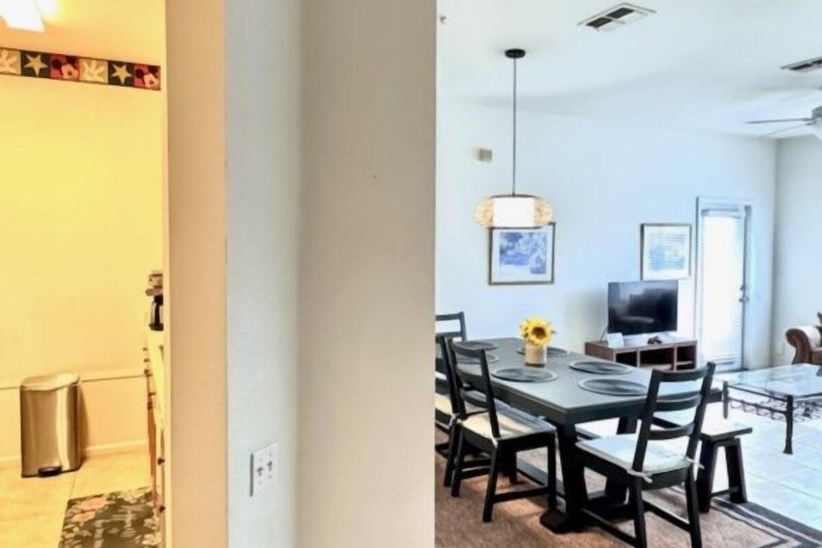 A dining area with a table and chairs, a television, and a patterned rug.