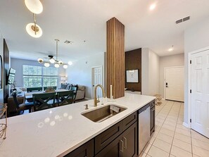 A modern kitchen with a central island, a built-in sink, and a dining area with a green table and chairs. - Windsor Palms 3 Bed Condo In Gated Resort 3 Bedroom Condo (Kissimmee)