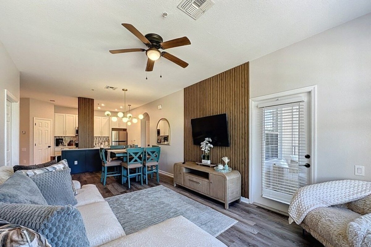 A modern living room with a sofa, TV, ceiling fan, and a dining area with chairs and a table.
