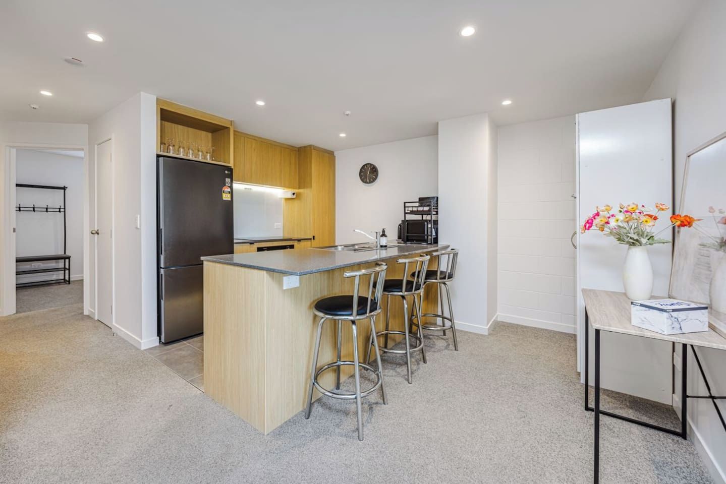 A modern kitchen with a central island, bar stools, a refrigerator, and a coffee machine.