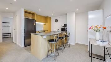 A modern kitchen with a central island, bar stools, a refrigerator, and a coffee machine.