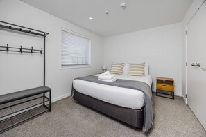 A bedroom with a bed, a bench, a bedside table, and a wardrobe. - Eden Vista Apartment 3 Bedrooms with free parking (Auckland)