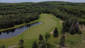 A golf course with a pond, surrounded by dense forest. - Welcome to Bellaire Base Camp at Shanty Creek Resorts, in Beautiful Bellaire, MI (Bellaire)