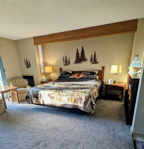 A bedroom with a large bed, a wooden headboard, a chair, a nightstand with a lamp, and a dresser. - Welcome to Bellaire Base Camp at Shanty Creek Resorts, in Beautiful Bellaire, MI (Bellaire)