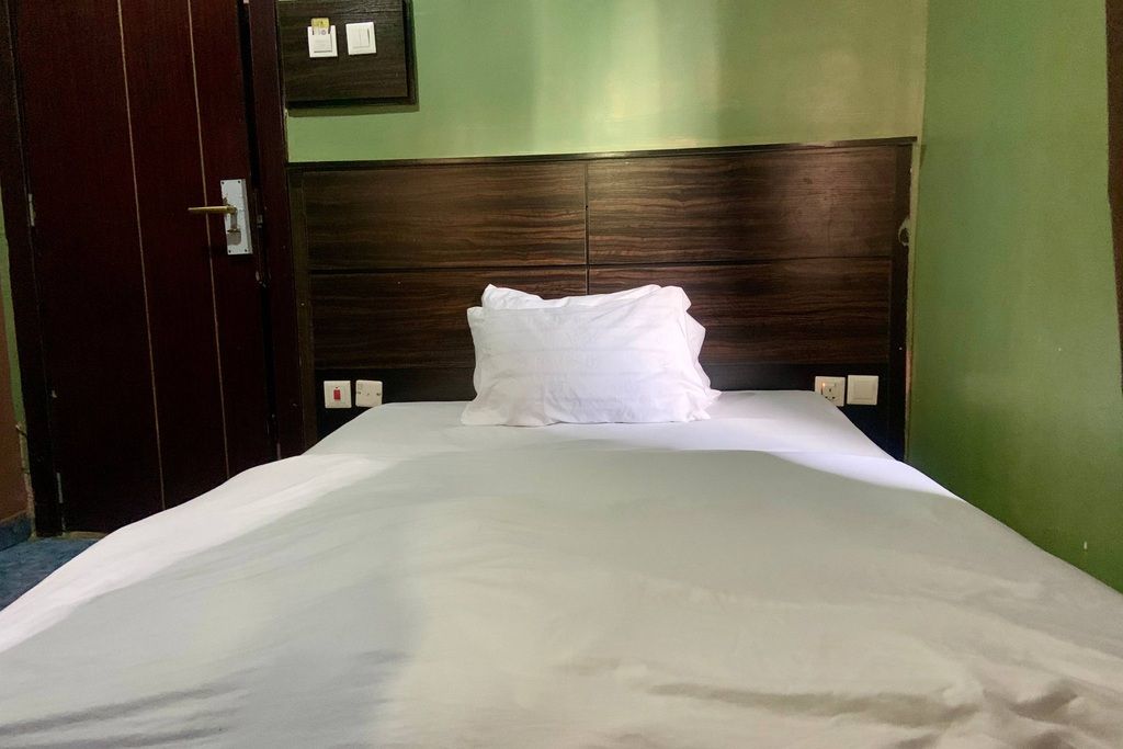 A neatly made bed with white linens and a single pillow, a wooden headboard, and a green wall.
