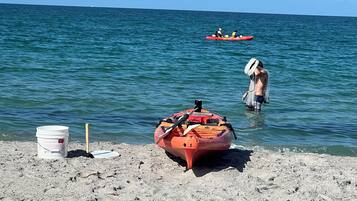 Una playa con un kayak rojo y un cubo blanco sobre la arena.