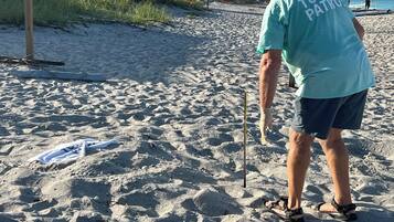 Uma praia arenosa com uma pessoa vestindo uma camiseta 'Turtle Patrol'.