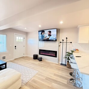 Una sala de estar moderna con un televisor de pantalla plana montado en la pared, una chimenea y una zona de cocina con encimera de mármol.