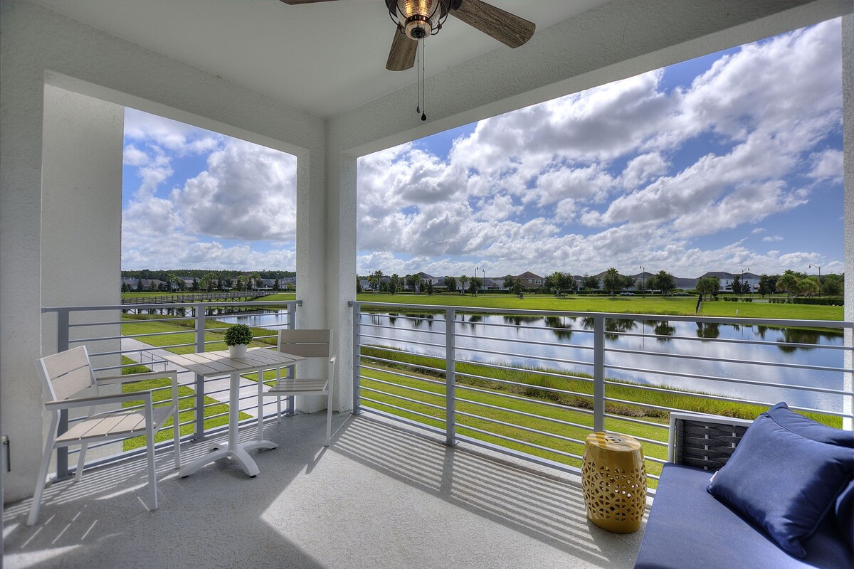 A balcony with a view of a lake, a table, and a chair.