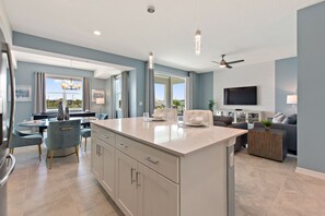 A modern kitchen with a central island, dining area with a piano, and a living room with a TV. - Fireworks @ Night -storey Lake By Shine Villas #709 2 Bedroom Condo (Kissimmee)