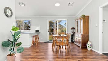 A modern kitchen with a dining area, wooden flooring, and a large window overlooking trees.