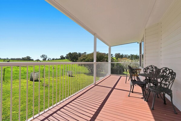 A covered outdoor area with a wooden deck, white railing, and metal chairs.