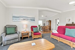 Ein Wohnzimmer mit einem grauen Sessel, einem roten Sofa, einem Holztisch und einem Meeresblick-Gemälde.