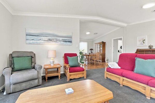 A living room with a grey armchair, a red sofa, a wooden coffee table, and a painting of a seascape.