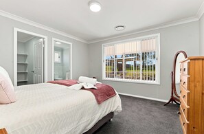 Ein Schlafzimmer mit Bett, Schrank, Fenster mit Aussicht und einer Tür zum Badezimmer.