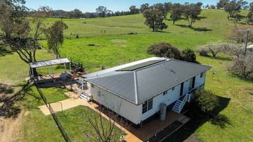 Una casa de un piso con techo de metal, rodeada por un patio cercado y un campo verde.
