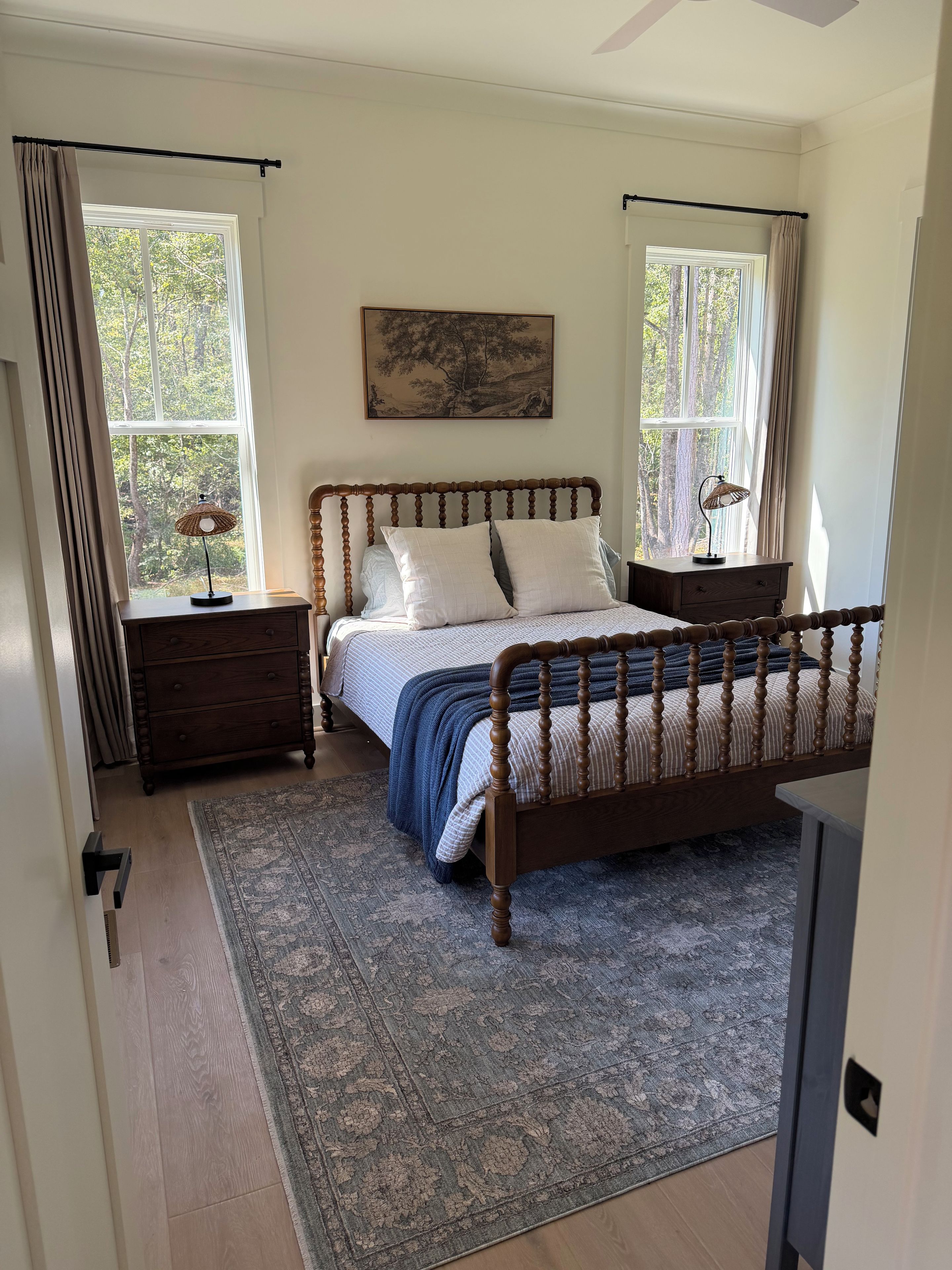 Une chambre à coucher avec un lit en bois, une table de chevet, une commode, un tapis et un tableau au mur.