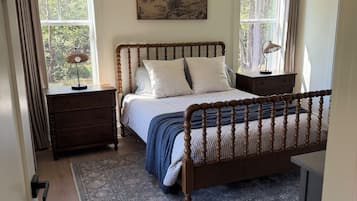 A bedroom with a wooden bed, a nightstand, a dresser, a rug, and a painting on the wall.