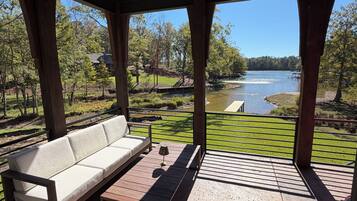 A covered outdoor seating area with a sofa and table, overlooking a lake and greenery.