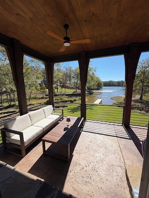 A covered outdoor seating area with a sofa and table, overlooking a lake and greenery. - Relaxing & Spacious Lake Life at NEW 'The Cove' (Alexander City)