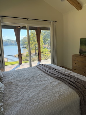 Un dormitorio con una cama grande, un aparador de madera y vistas a un lago a través de una puerta corrediza de vidrio.