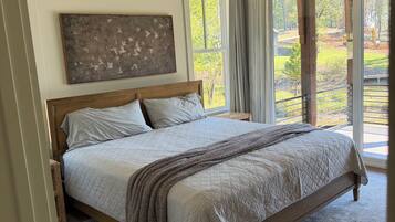 A bedroom with a large bed, a ceiling fan, a view of the outdoors, and a painting on the wall.