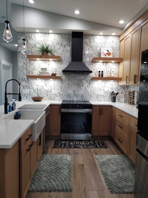 A modern kitchen with marble backsplash, wooden cabinets, stainless steel appliances, and pendant lighting.