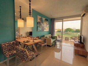 A modern living room with a dining area, a sofa, and a TV. There is a large window with a view of the outdoors. - Atlantis resort condo Pattaya - One bedroom & living room all included apartment (Muang Pattaya)