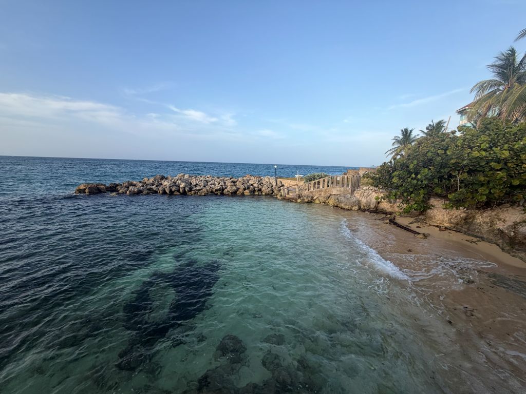 Un paysage côtier avec une eau claire, une digue rocheuse et une plage de sable.