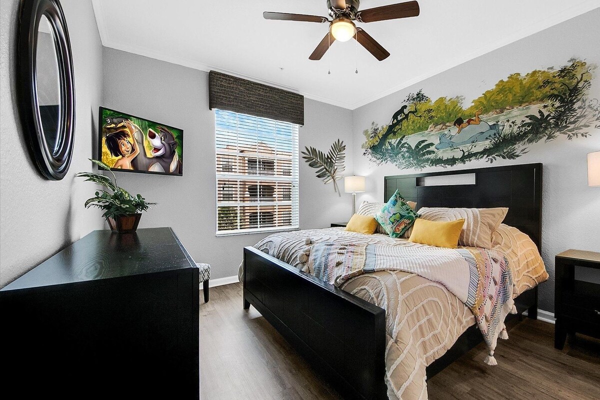 A bedroom with a bed, bedside tables, a ceiling fan, a window with blinds, and a wall mural.