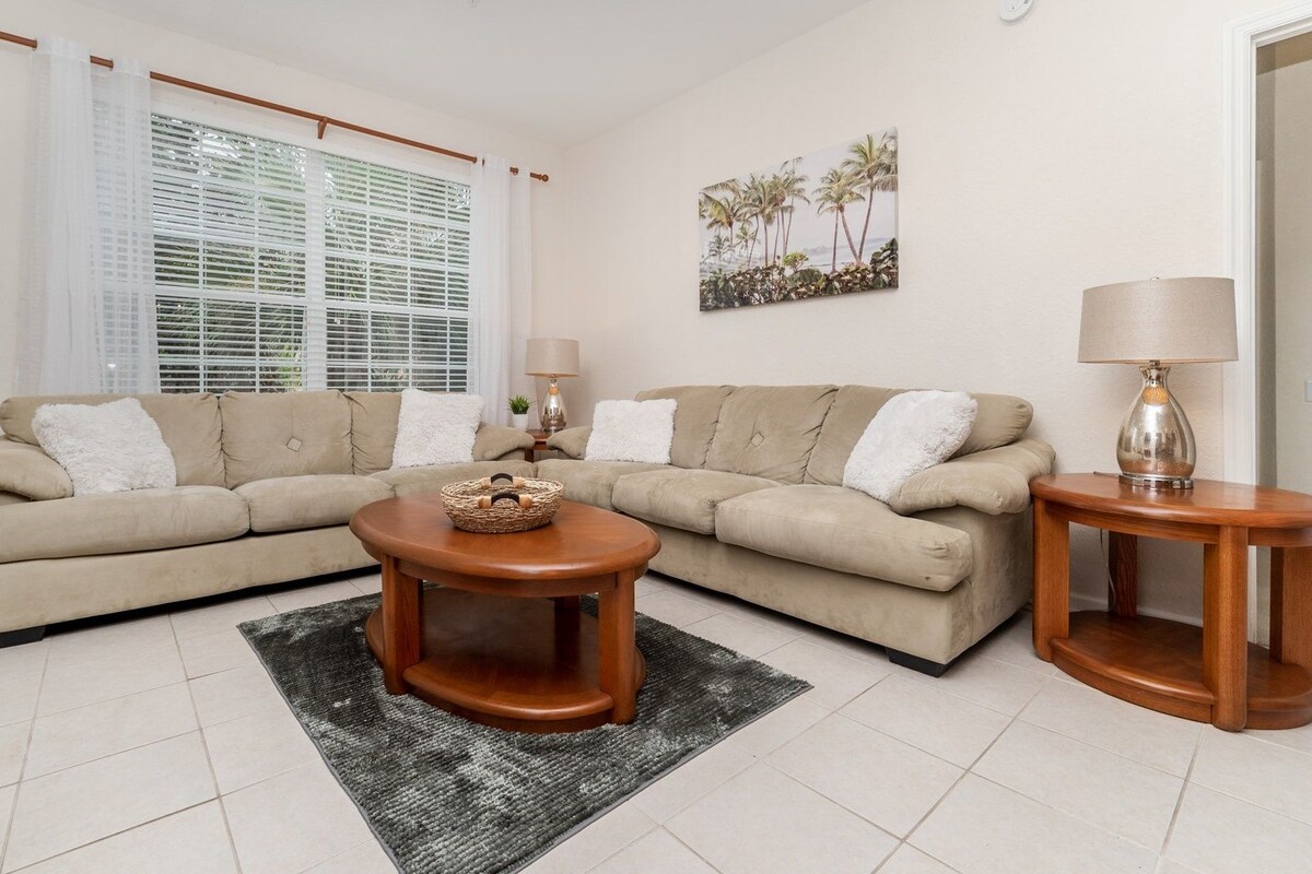 A living room with a beige sectional sofa, a round wooden coffee table, and a side table with a lamp.