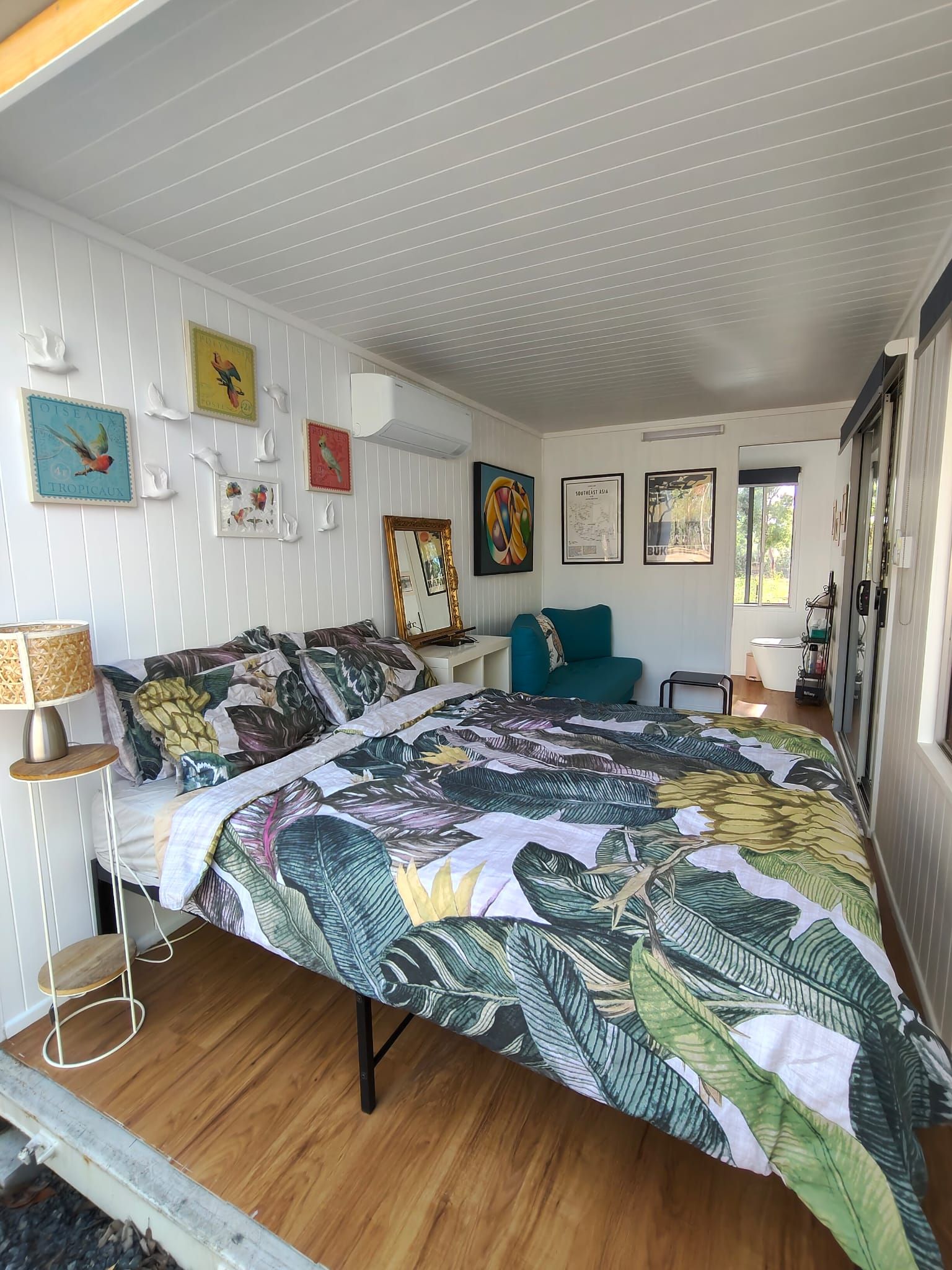 Een slaapkamer met een groot bed, een staande lamp, een klein tafeltje en een raam.