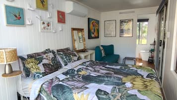 Een slaapkamer met een groot bed, een staande lamp, een klein tafeltje en een raam.