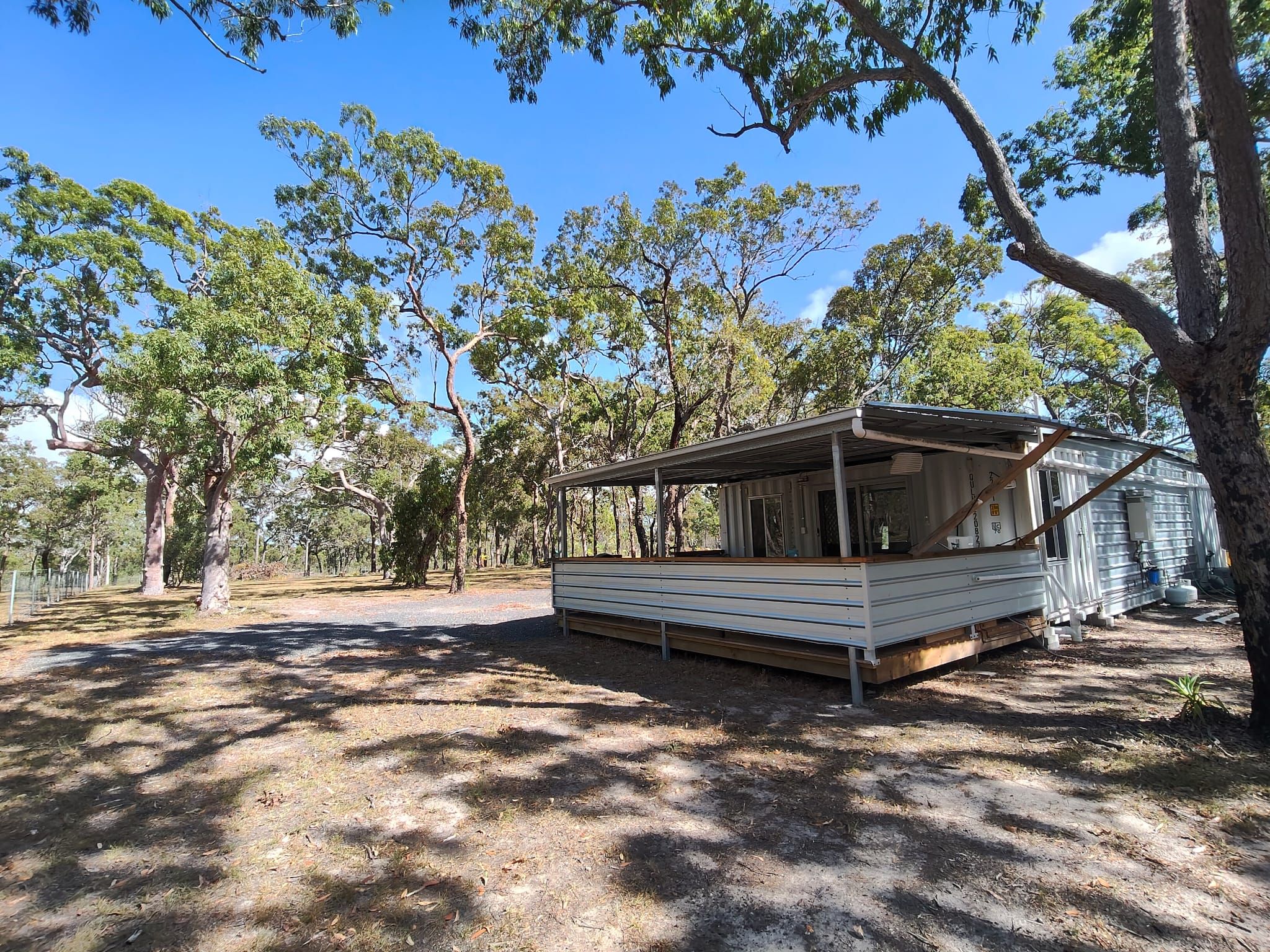 A mobile home with a covered porch, surrounded by trees and a fenced area.