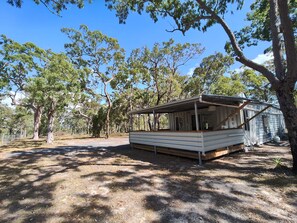 A mobile home with a covered porch, surrounded by trees and a fenced area.