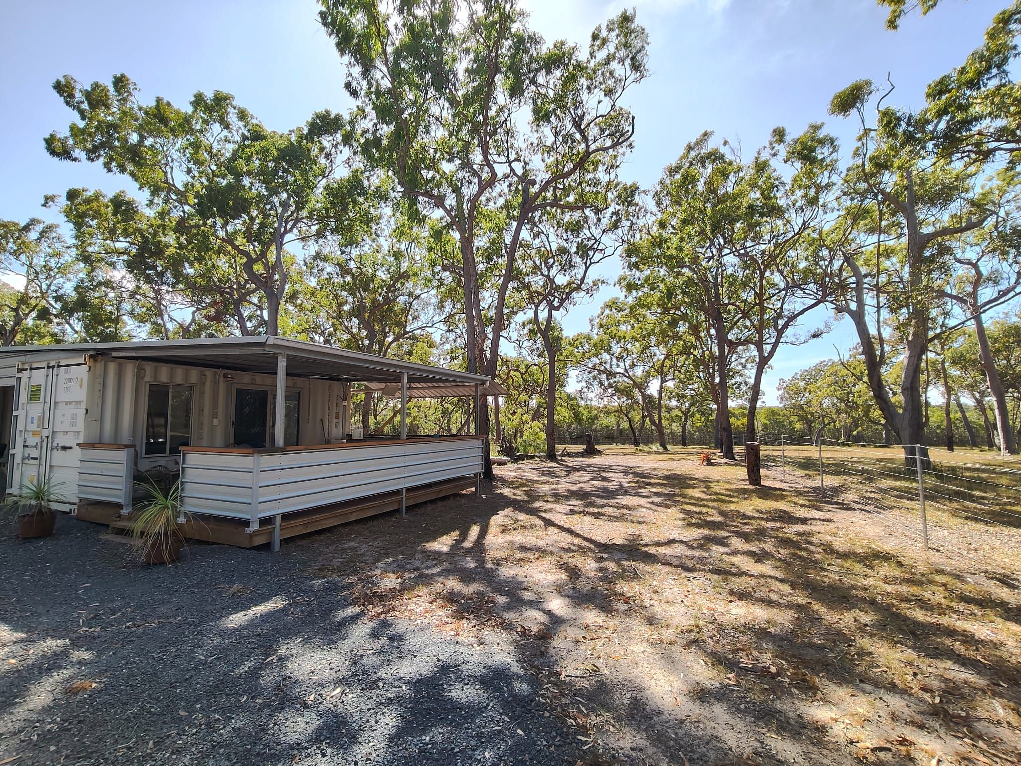 A small cabin with a porch, surrounded by trees in a dry, gravelly area.