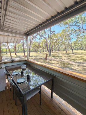 An outdoor dining area with a glass table and chairs, a view of a tree-lined park.