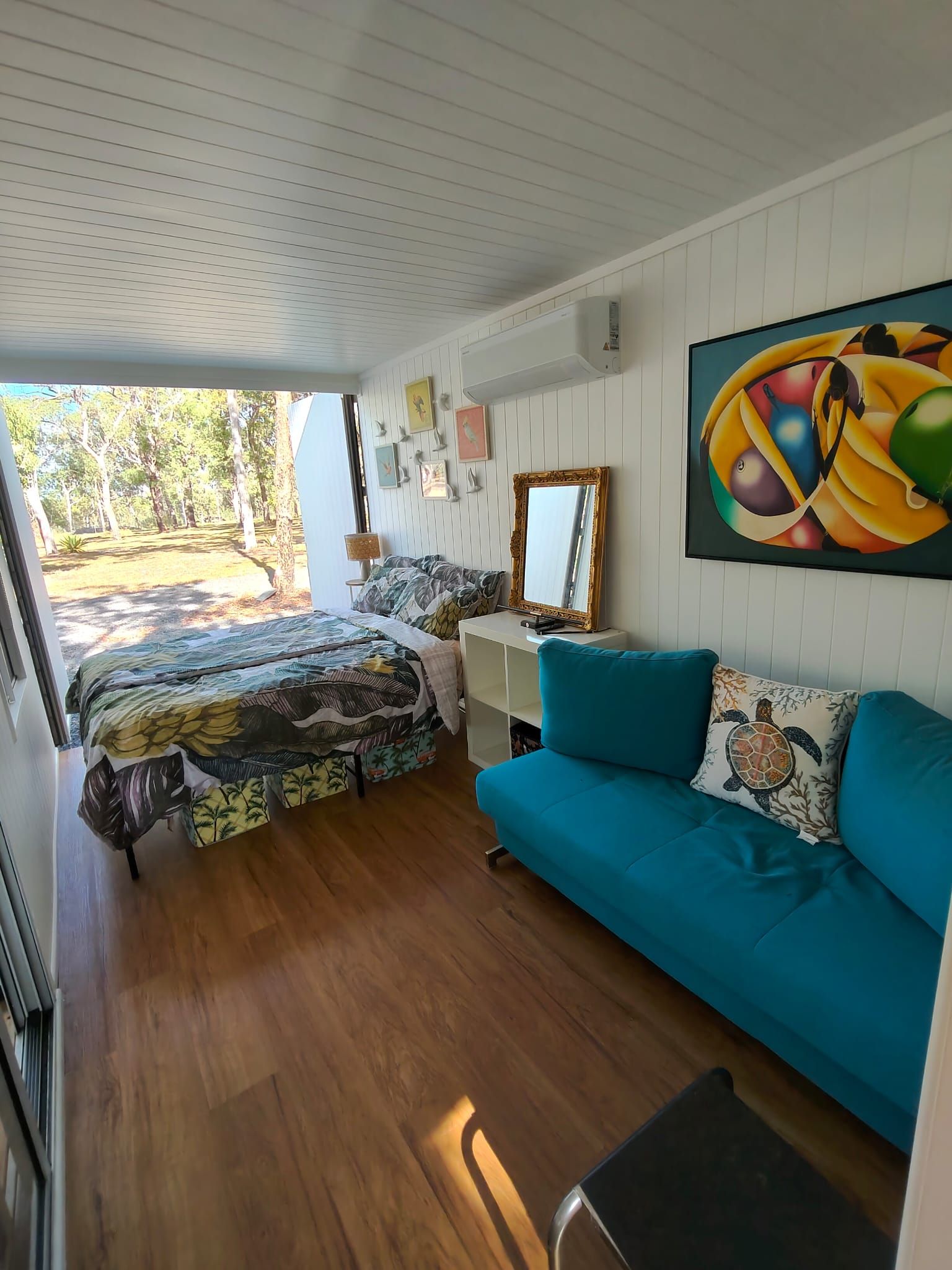 A room with a bed, a sofa, a mirror, and a painting on the wall.