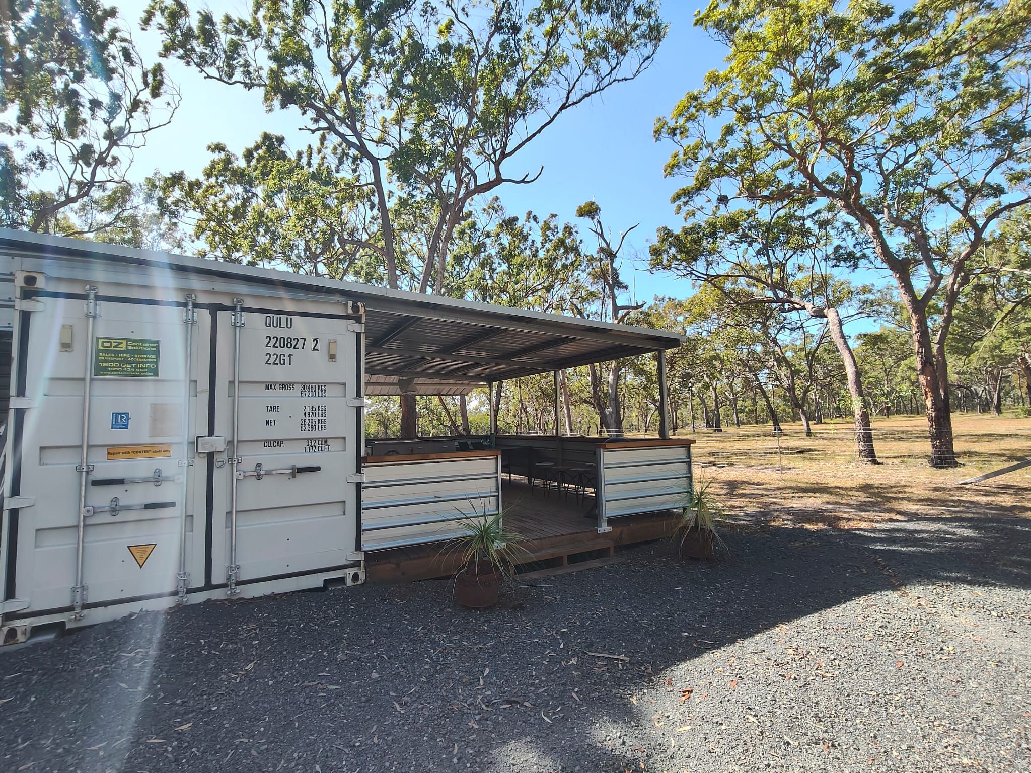 A container with a roofed area, possibly a temporary structure, in a natural setting with trees.