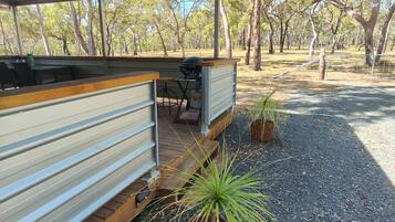 A covered outdoor seating area with a grill, surrounded by trees and gravel.