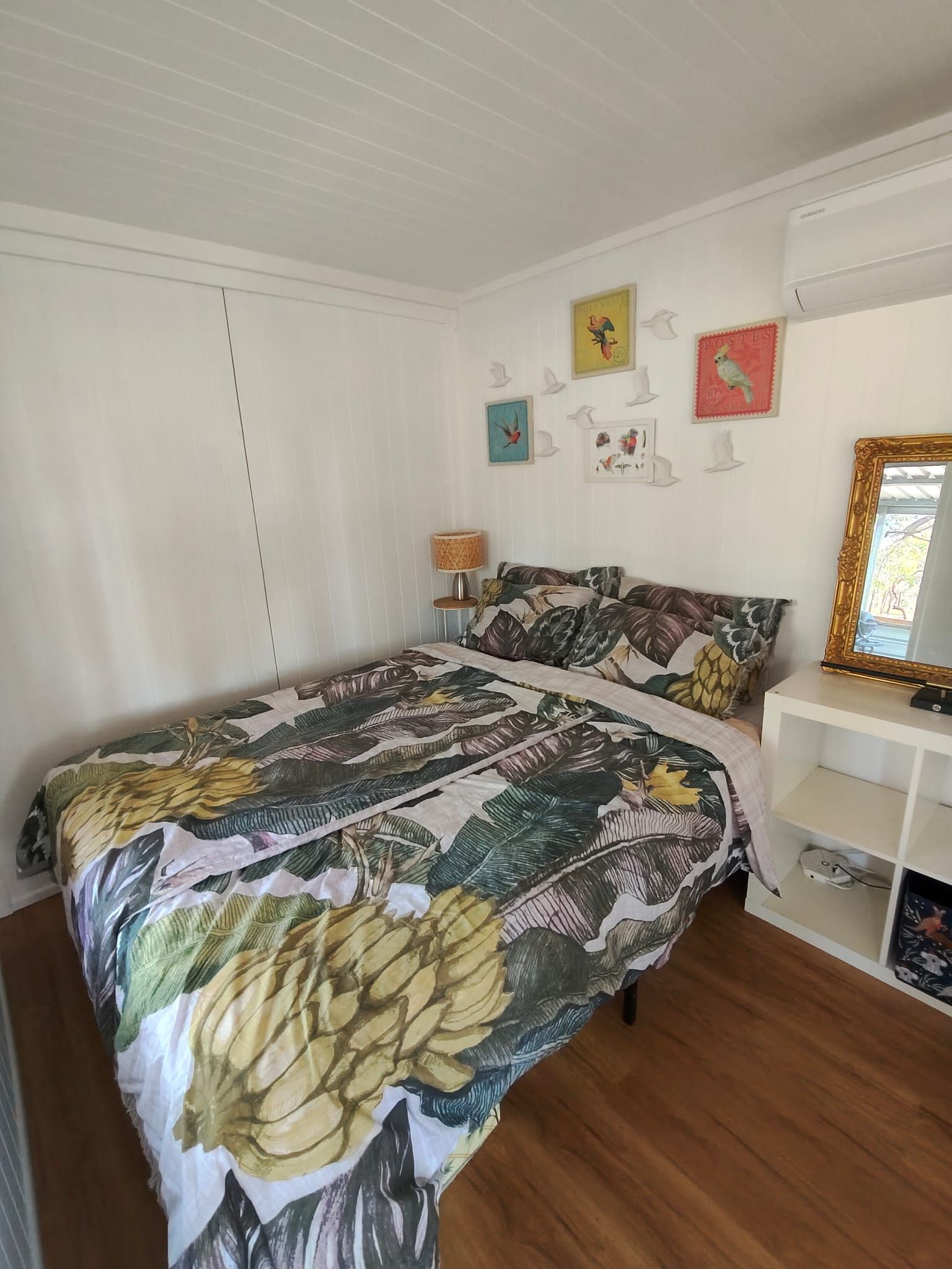 A bedroom with a bed, a nightstand, a lamp, a dresser, and wall decorations including framed pictures and a mirror.