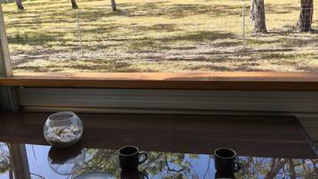 Ein Esstisch mit Tellern, einer Schüssel und einer Tasse, vor einem Fenster mit Blick auf eine bewaldete Landschaft.