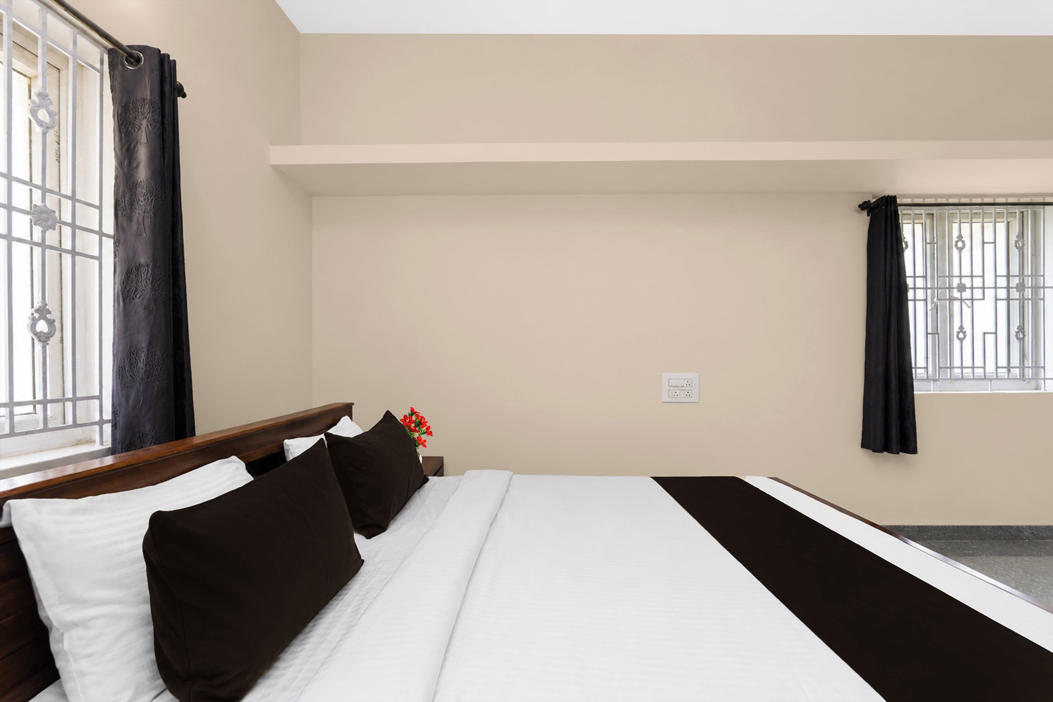 Una habitación de hotel con cama, mesita de noche, ventana con cortinas y toma de corriente.