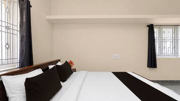 Una habitación de hotel con cama, mesita de noche, ventana con cortinas y toma de corriente.